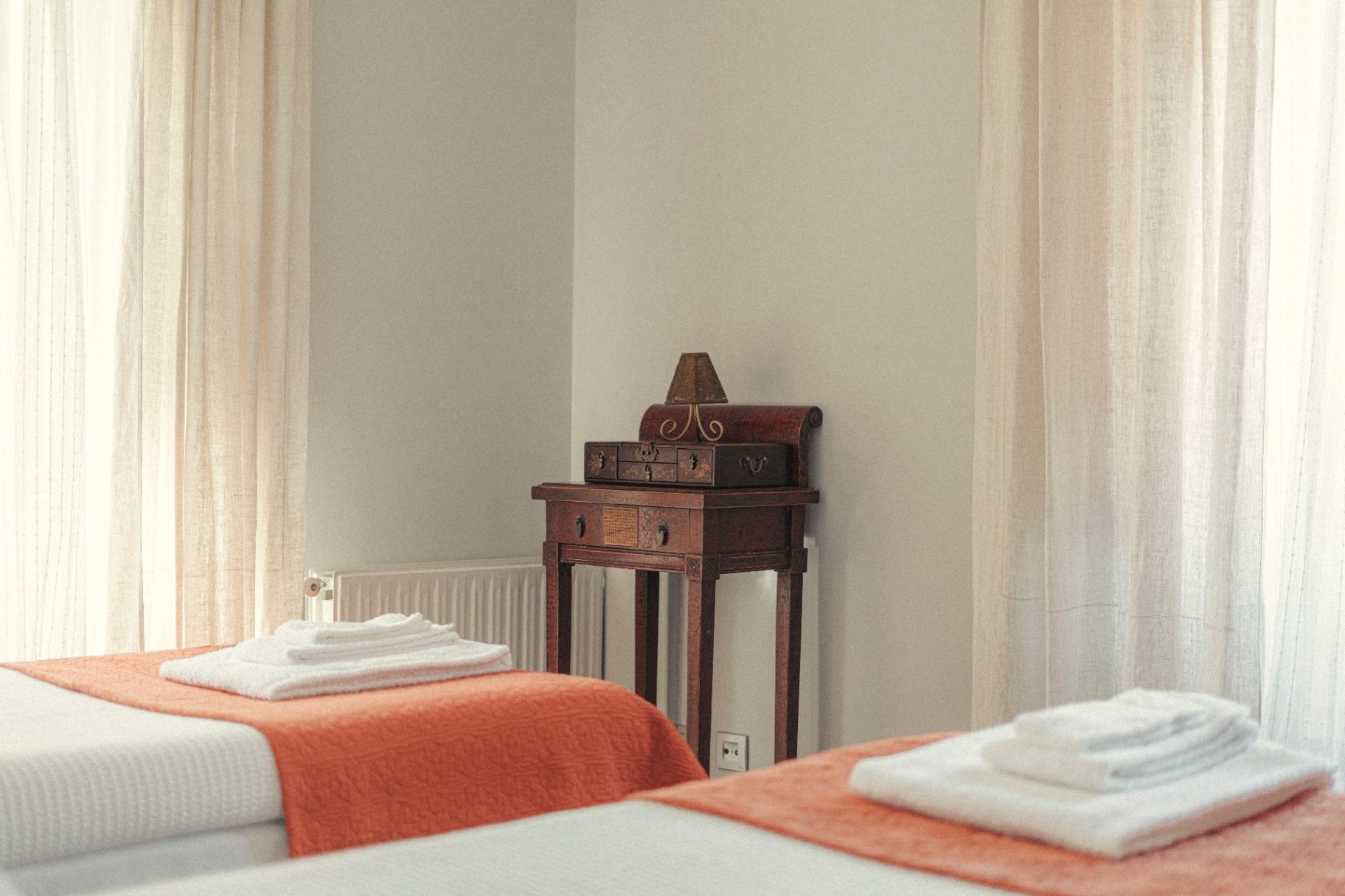 Twin beds with terracotta throws and antique lacquered side table